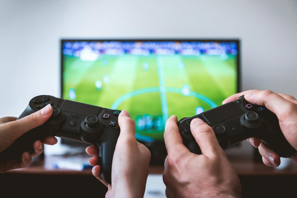 Two Playstations controllers being used in front of a football game displayed on a television